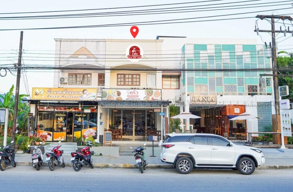 Street view of a row of shops with parked motorbikes and a white SUV in front, featuring a massage parlor, a restaurant, and a modern teal building.