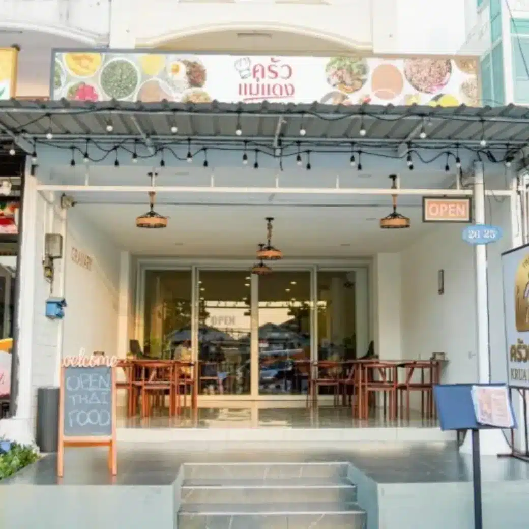 Front view of a Thai restaurant with a sign, a chalkboard reading "OPEN THAI FOOD," string lights, and visible tables and chairs inside.