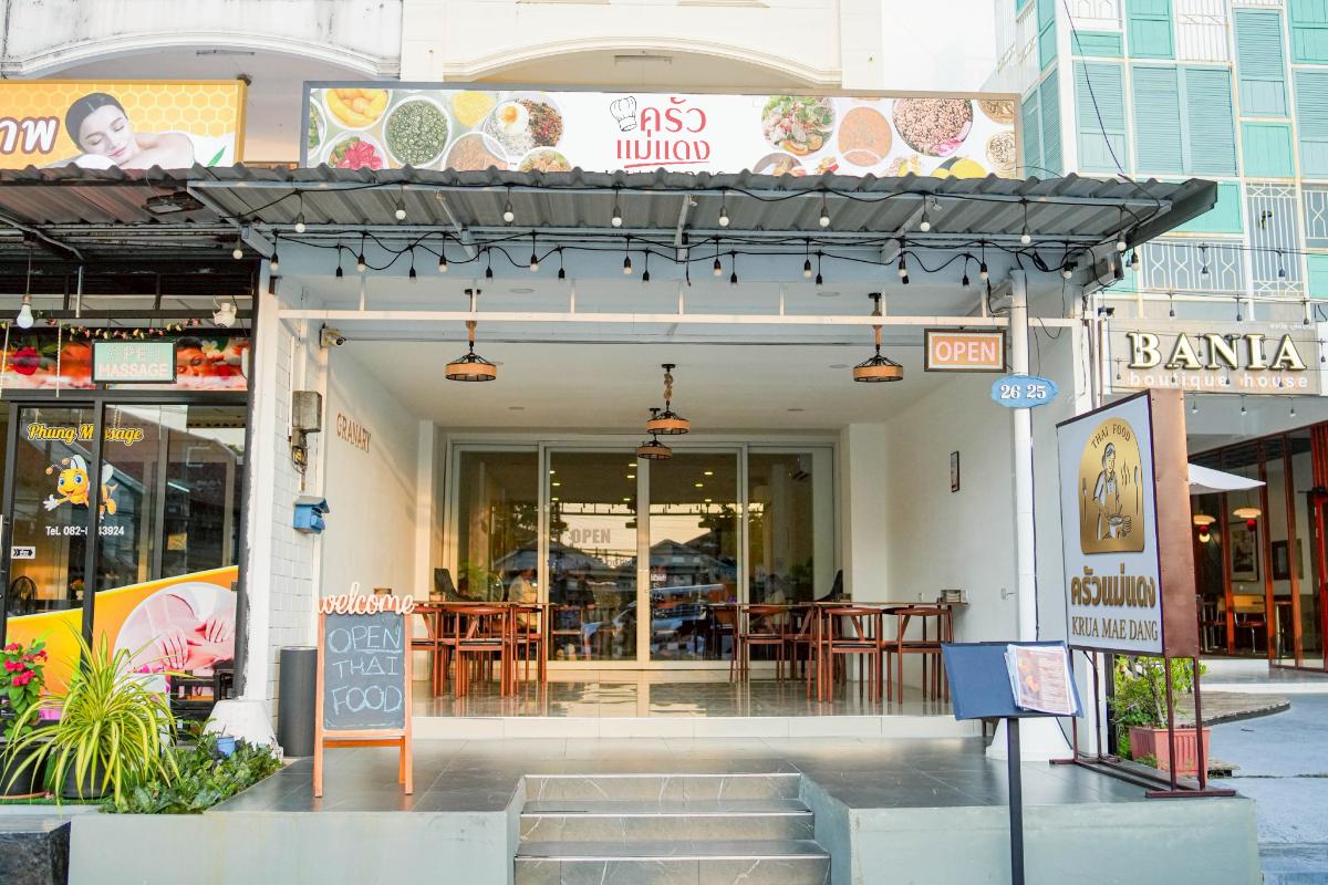 Street view of a Thai restaurant with tables and chairs inside, an "OPEN" sign, and a chalkboard advertising "OPEN THAI FOOD" at the entrance.