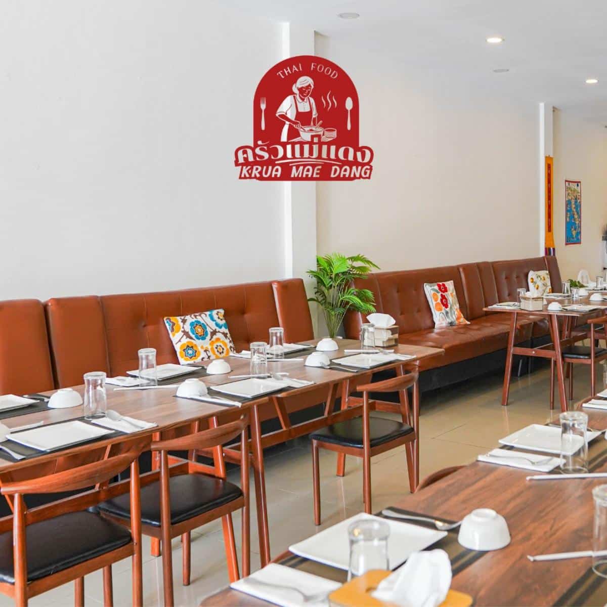 A modern Thai restaurant interior with brown seating, set dining tables, and a "Krua Mae Dang" logo on the wall.